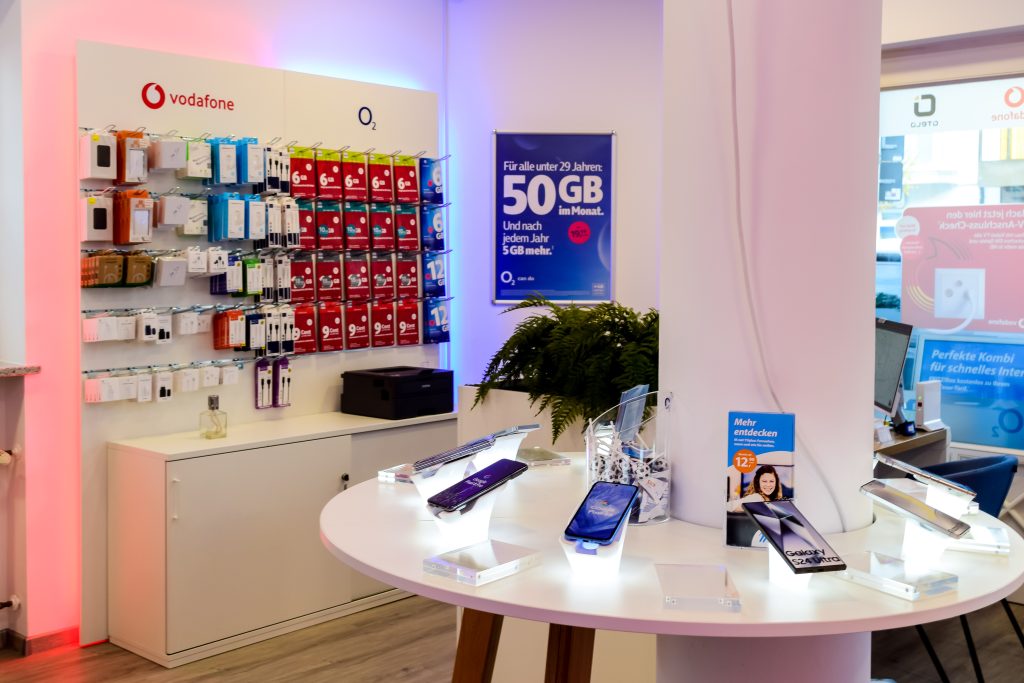 Wand mit Vodafone und O2 Produkten sowie einem Tisch mit Displays im Geschäft.