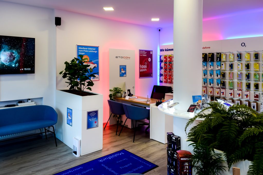 Verkaufsraum von ETOCOM mit blauen Stühlen, Pflanzen und Produktdisplays an der Wand.