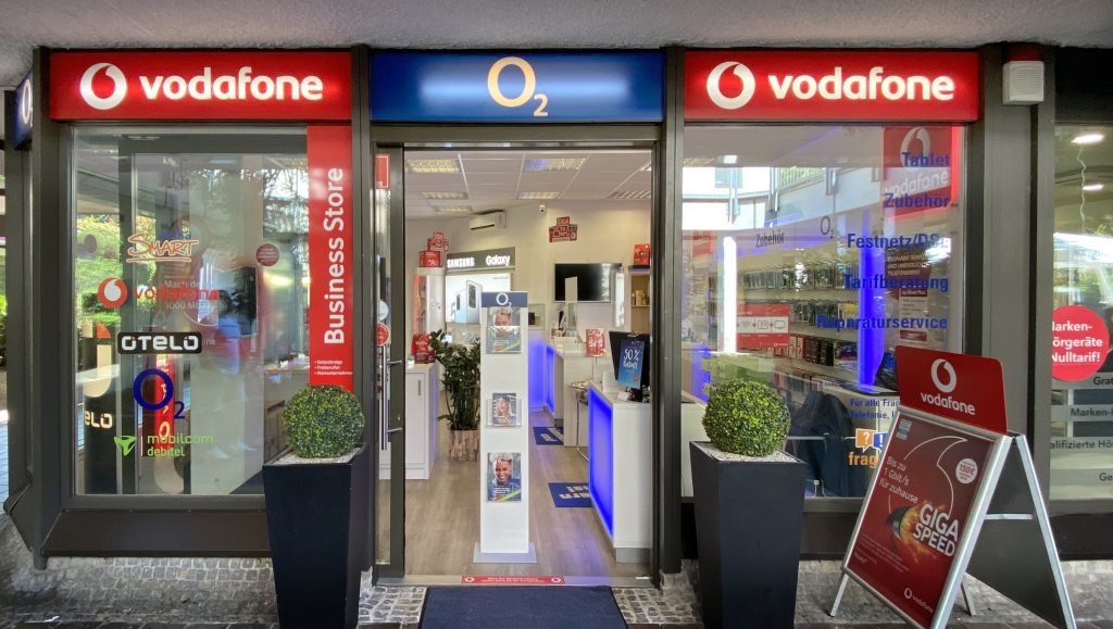 Eingang zu einem Vodafone O2 Geschäftsladen mit beleuchtetem Logo und Schaufenster.